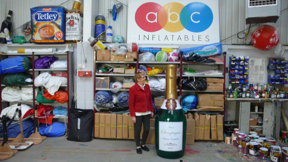 Woman standing next to 6 foot inflatable Champagne bottle
