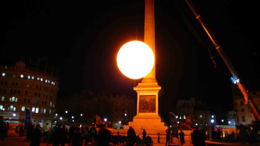 Giant glowing inflatable being lifted by crane beside Nelson's Column